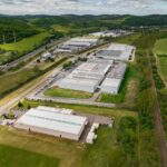 Industrial warehouse complex aerial view, logistics distribution center, green valley landscape, modern infrastructure, sunny day